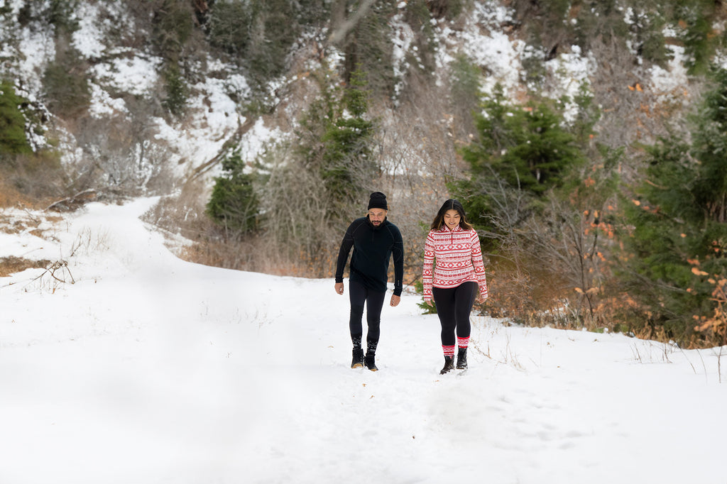 Two people wearing Hot Chillys Base Layers hiking up a snowy mountain road